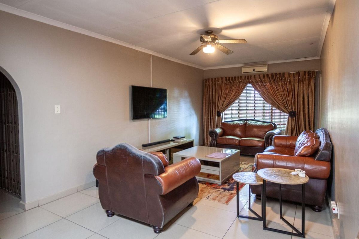 A comfortable living room featuring tiled flooring, a ceiling fan, and a wall-mounted air conditioning unit, with an arched entryway leading to other areas.