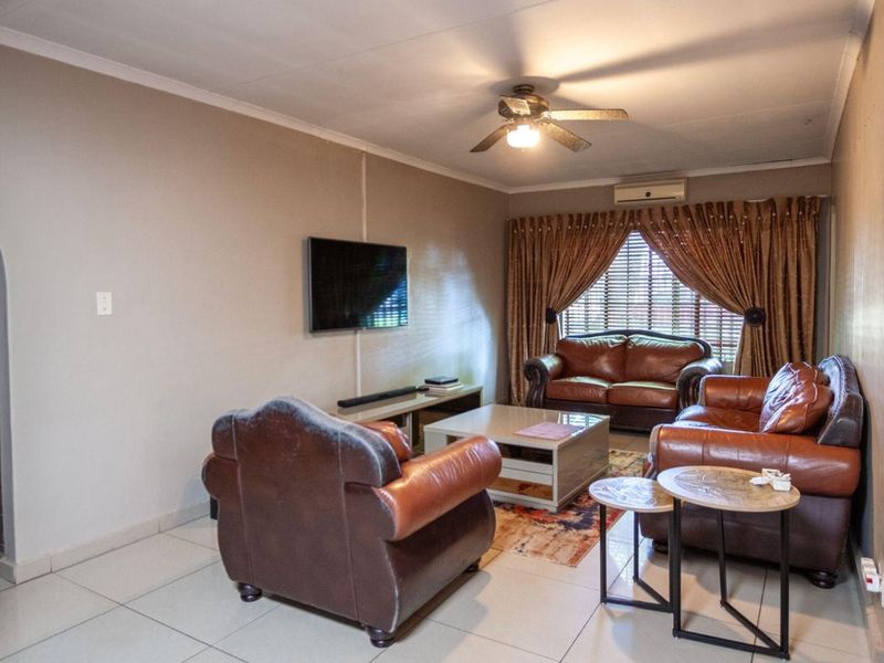 A comfortable living room featuring tiled flooring, a ceiling fan, and a wall-mounted air conditioning unit, with an arched entryway leading to other areas.