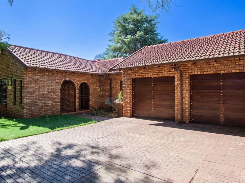 Front elevation of a brick house featuring a double garage, paved driveway, and tiled roof, set within a landscaped garden.