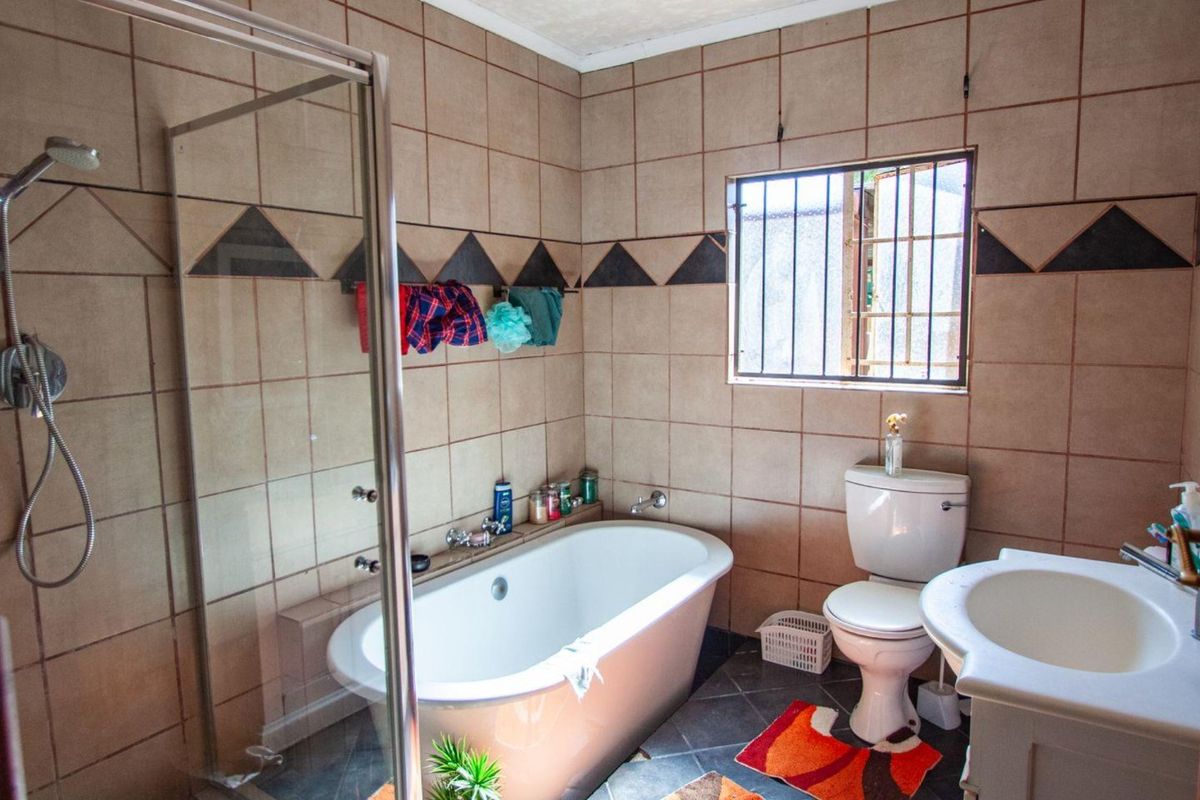 A functional bathroom featuring a freestanding bathtub, separate glass-enclosed shower, pedestal basin, and toilet, finished with neutral wall tiling and dark floor tiles.