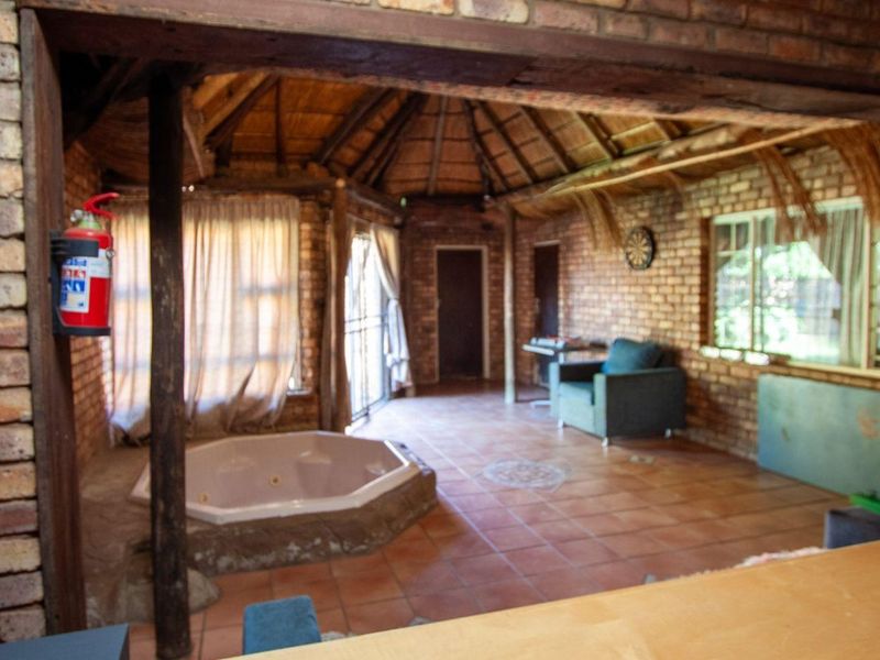 Rustic living area featuring exposed brick walls, a thatched roof, terracotta flooring, and a built-in spa bath.