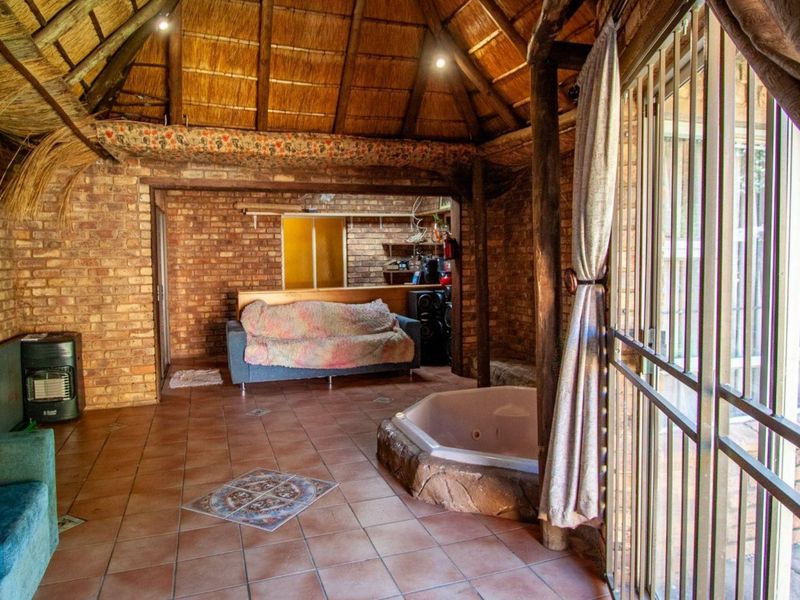 Rustic living area featuring exposed brick walls, a traditional thatched ceiling, tiled flooring, and a built-in spa bath with direct access to the exterior.