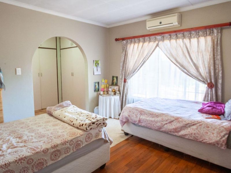 A spacious bedroom featuring timber flooring, a split-system air conditioner, and an arched entryway leading to built-in storage cupboards.
