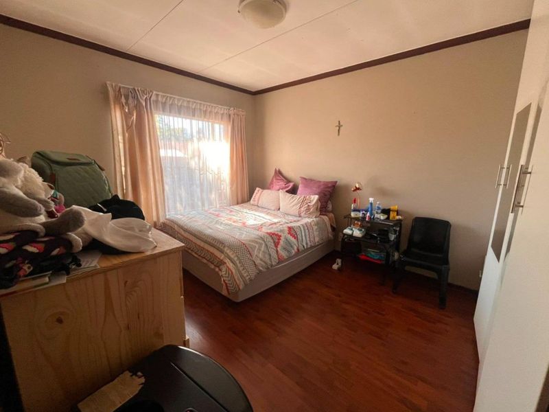 A standard bedroom featuring laminate flooring, a built-in wardrobe, and a window with curtains, providing a functional living space.
