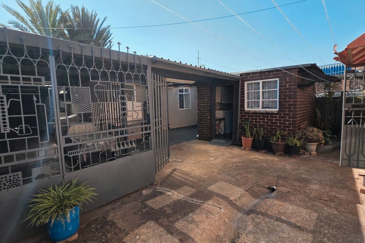 A rear exterior view of the property featuring brick walls, concrete paving, and secure metal gates.