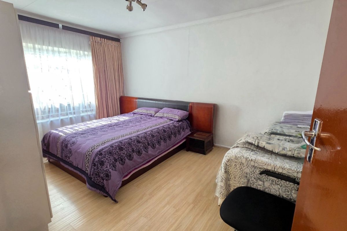 A functional bedroom featuring laminate flooring, a built-in wardrobe, and natural light through a window with curtain rails.