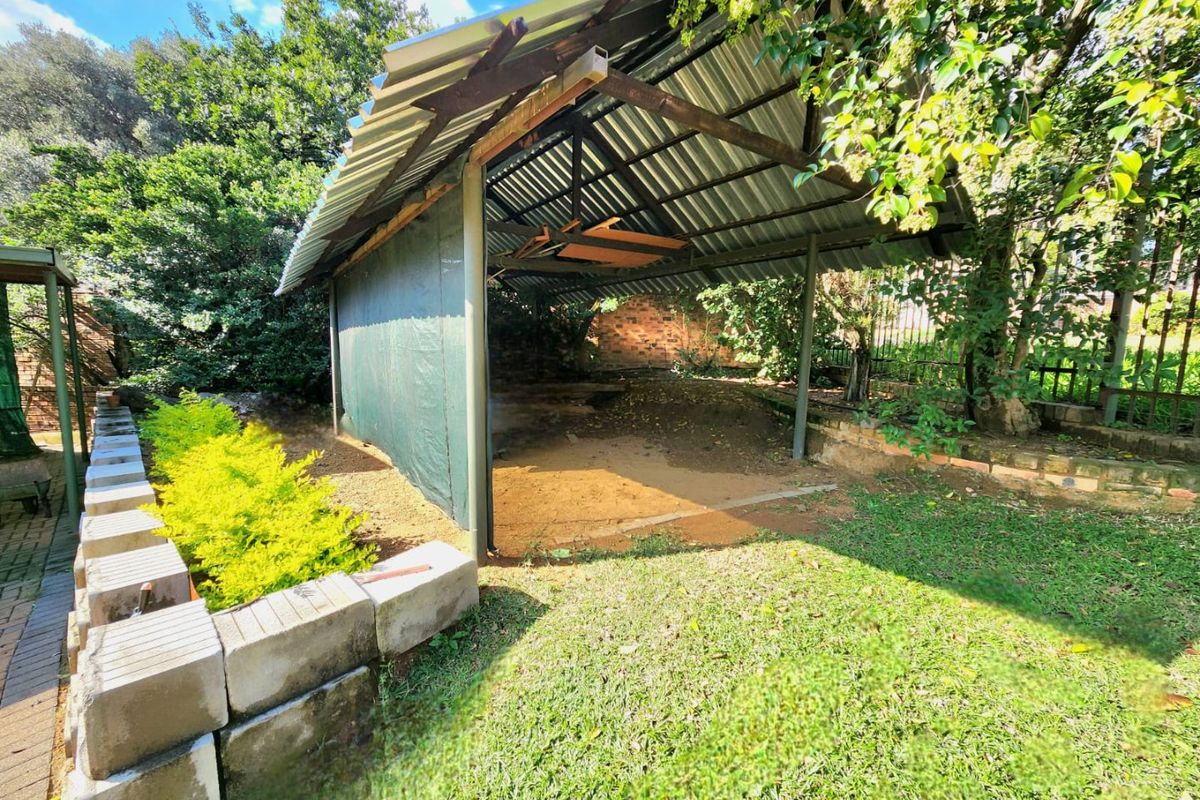 A basic outdoor shelter structure with a corrugated metal roof, situated in a garden area with brick and concrete block landscaping elements.