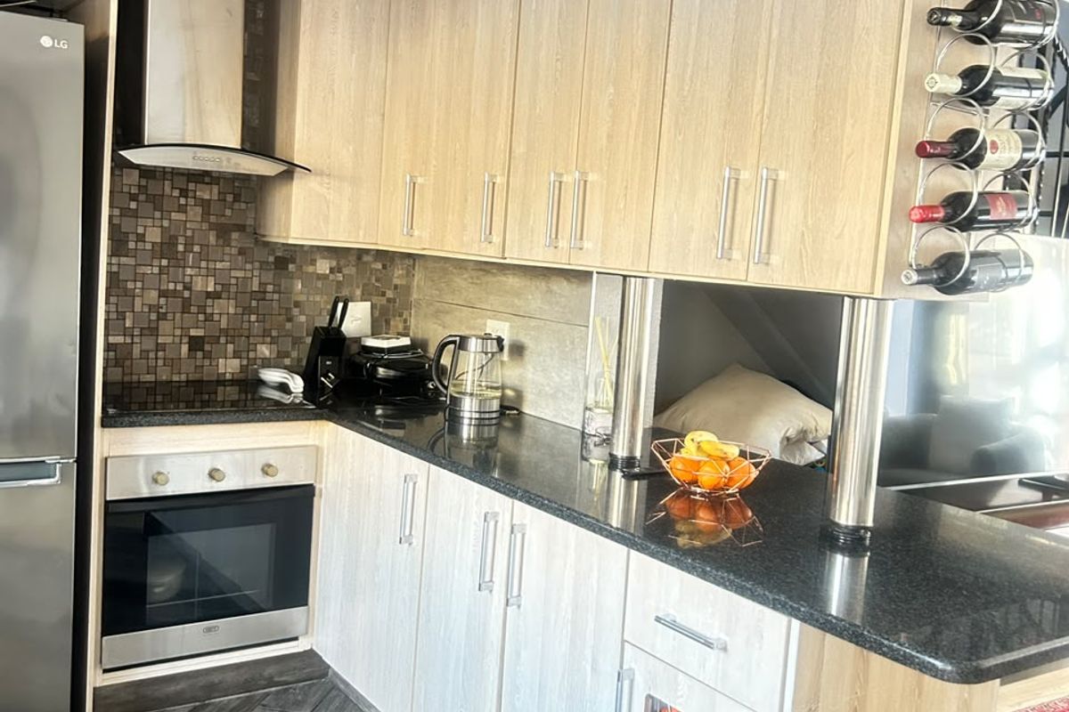 Modern kitchen featuring light wood cabinetry, granite countertops, mosaic tile backsplash, and integrated appliances including an oven, hob, and wine cooler.