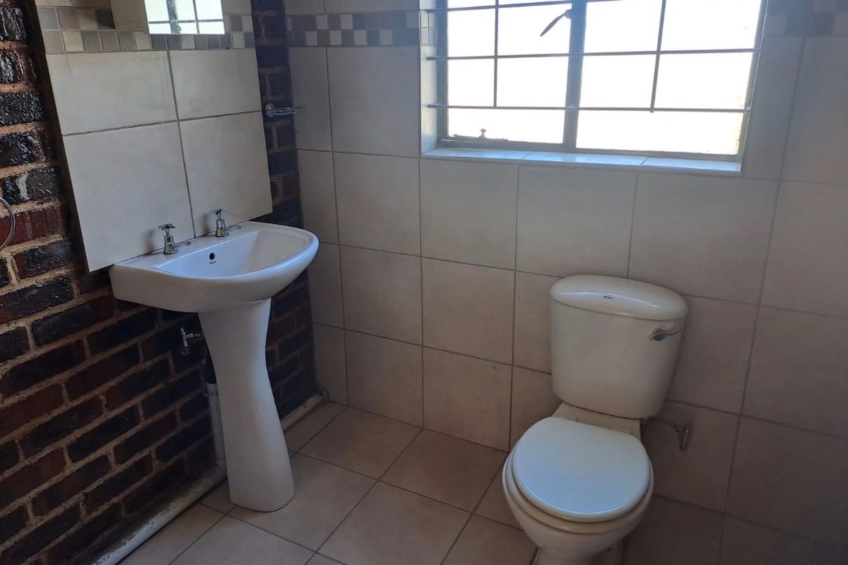 A compact bathroom featuring a pedestal basin, toilet, and tiled finishes, requiring cosmetic updates to improve its overall condition and aesthetic appeal.
