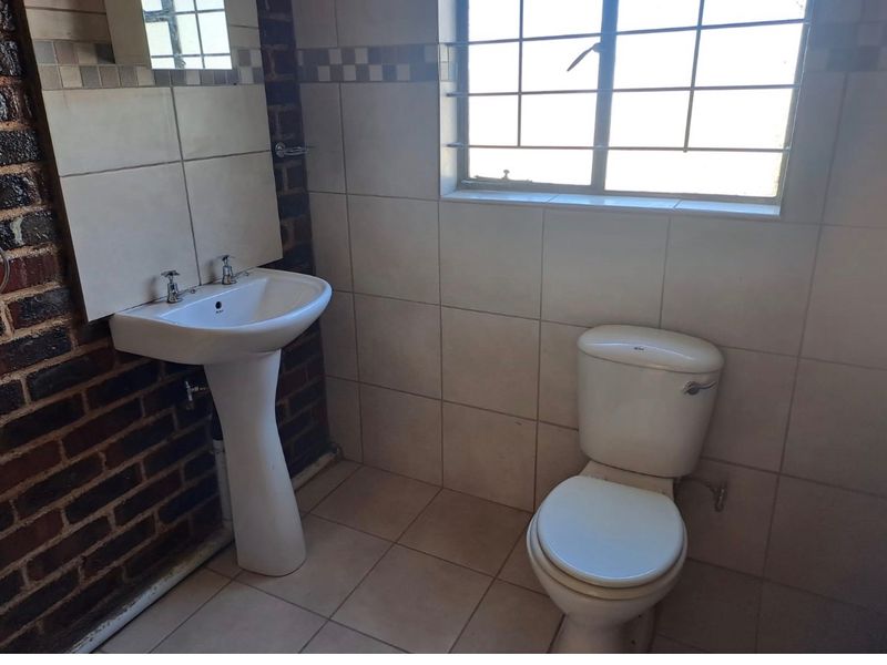 A compact bathroom featuring a pedestal basin, toilet, and tiled finishes, requiring cosmetic updates to improve its overall condition and aesthetic appeal.