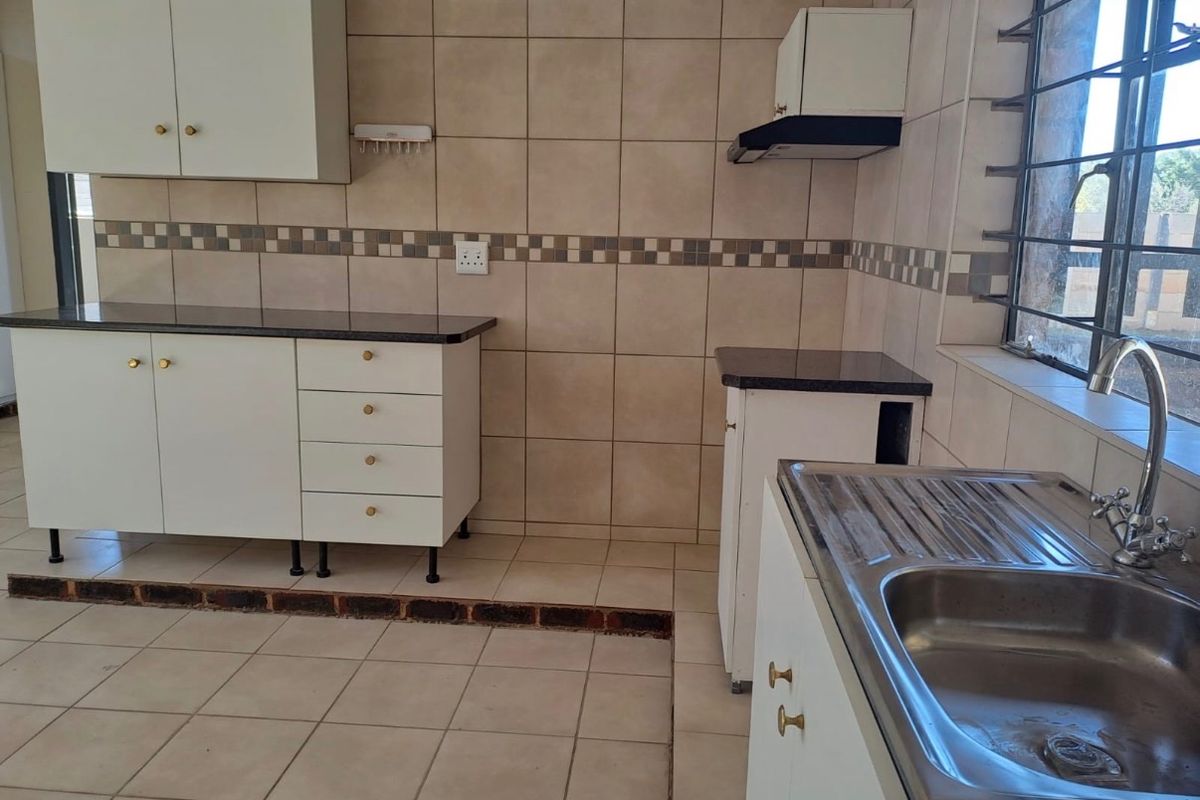 A functional kitchen featuring white cabinetry, granite countertops, a stainless steel sink, and tiled finishes, offering a clean space ready for personalization.