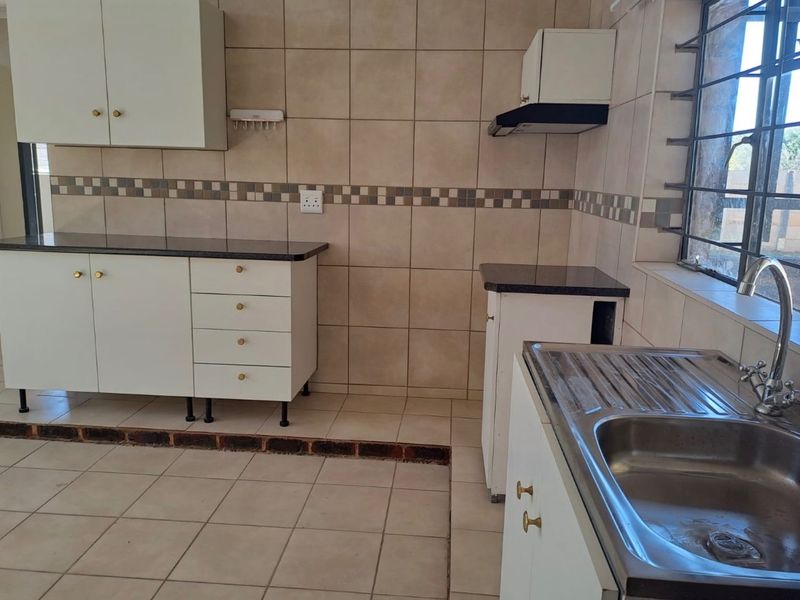 A functional kitchen featuring white cabinetry, granite countertops, a stainless steel sink, and tiled finishes, offering a clean space ready for personalization.