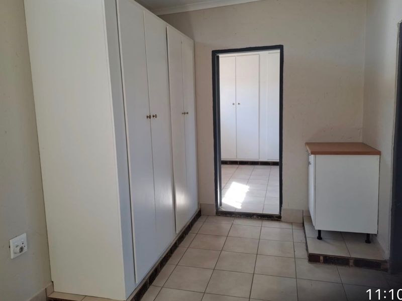 A functional scullery or utility area featuring built-in storage cupboards, tiled flooring, and a small base cabinet with a laminate countertop.