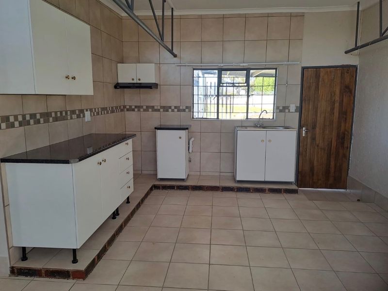 A functional kitchen area featuring tiled walls and floors, built-in cabinetry with granite countertops, and a stainless steel sink.