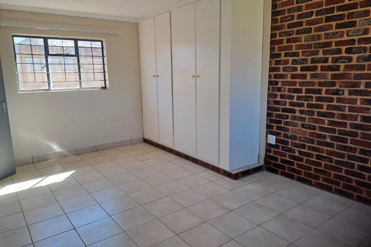 A bright, empty bedroom featuring tiled flooring, built-in cupboards, and an exposed brick feature wall, providing a versatile space for customization.