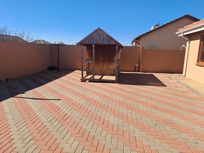 A paved rear courtyard featuring a boundary wall and a detached wooden storage shed.