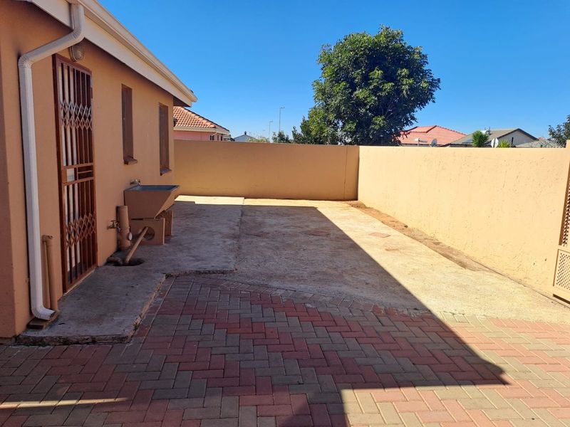 A rear exterior area featuring a combination of concrete and brick paving, a perimeter wall, and a utility sink.