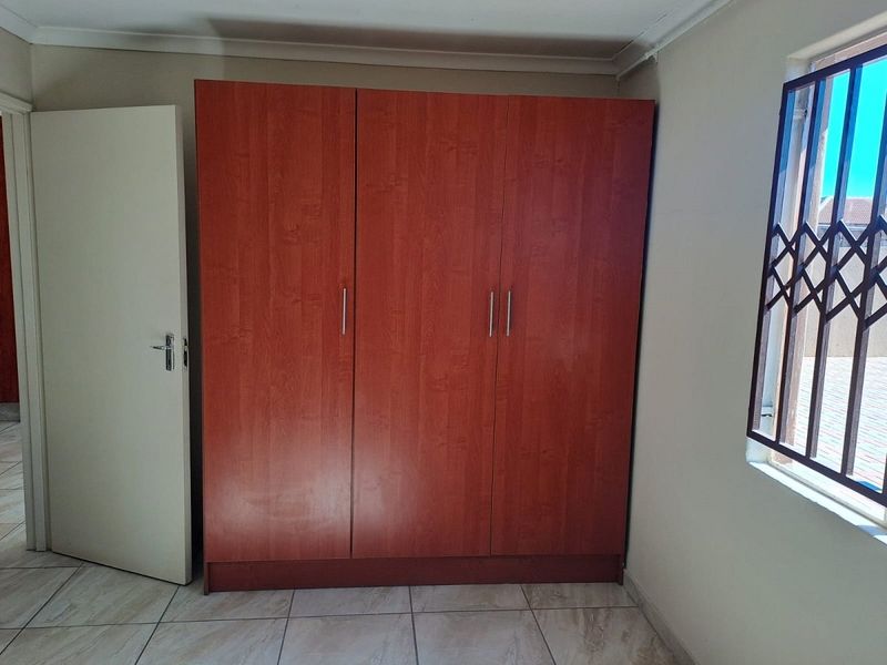 A bedroom featuring a built-in wooden wardrobe, tiled flooring, and a window fitted with a security gate.