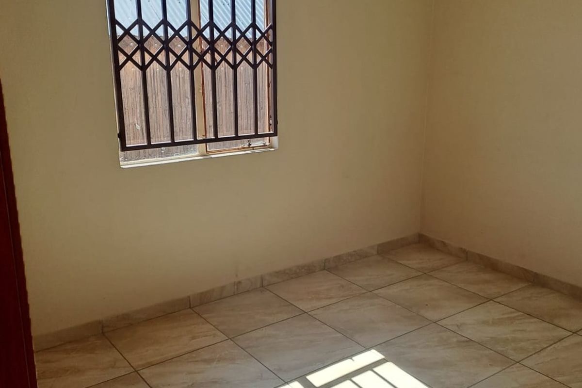 An empty bedroom featuring tiled flooring and security bars on the window, providing a blank canvas for potential renovation or staging.