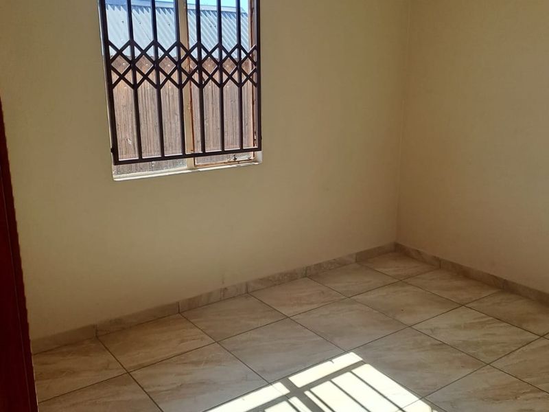 An empty bedroom featuring tiled flooring and security bars on the window, providing a blank canvas for potential renovation or staging.