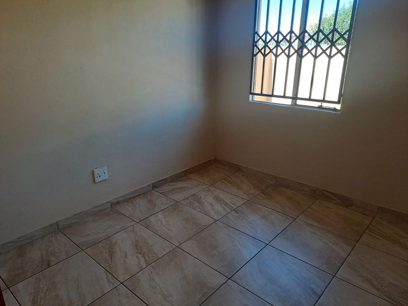 An empty bedroom featuring neutral tiled flooring and a window fitted with a security gate.