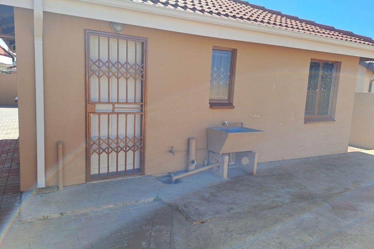 Rear exterior view of the property featuring a concrete laundry trough, security gate, and paved outdoor area.