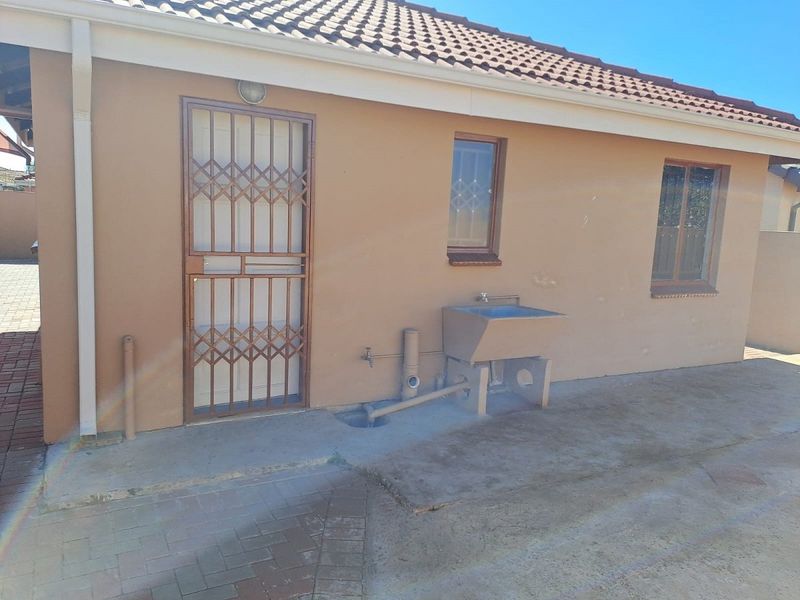 Rear exterior view of the property featuring a concrete laundry trough, security gate, and paved outdoor area.