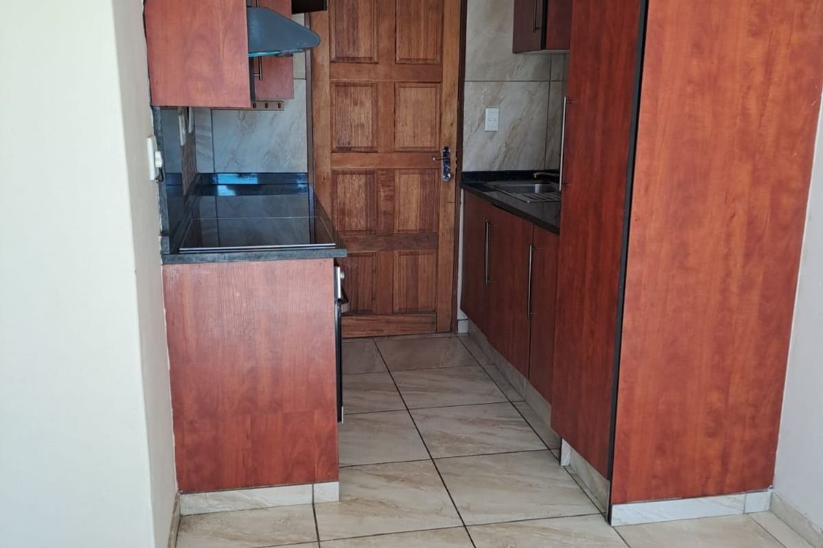 A compact kitchen featuring laminate cabinetry, granite countertops, tiled flooring, and a tiled backsplash, providing a functional workspace.