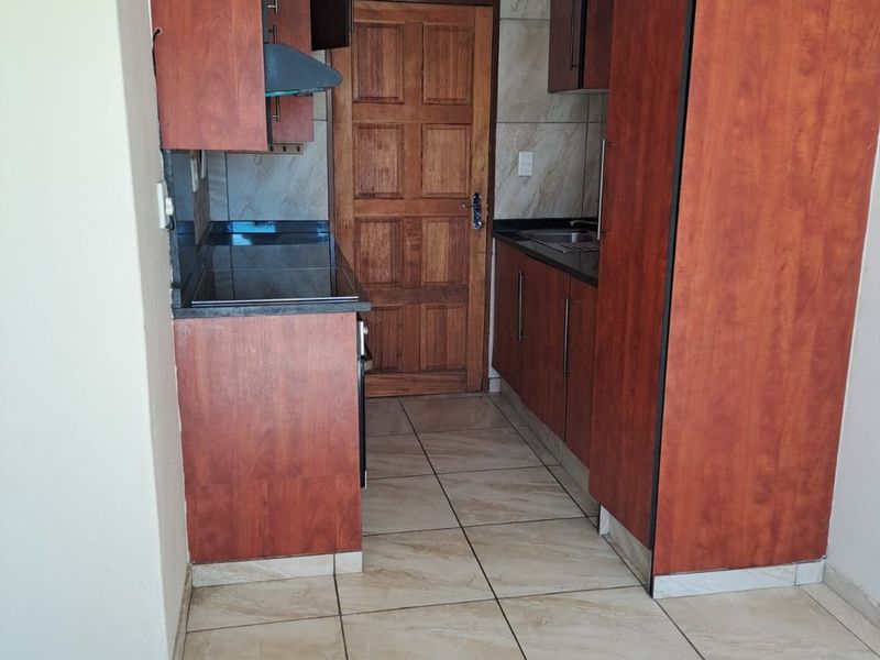 A compact kitchen featuring laminate cabinetry, granite countertops, tiled flooring, and a tiled backsplash, providing a functional workspace.