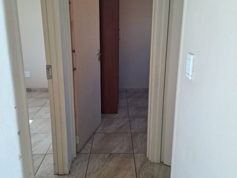 A view through a hallway featuring neutral tiled flooring and access to an adjacent room with a built-in cupboard.
