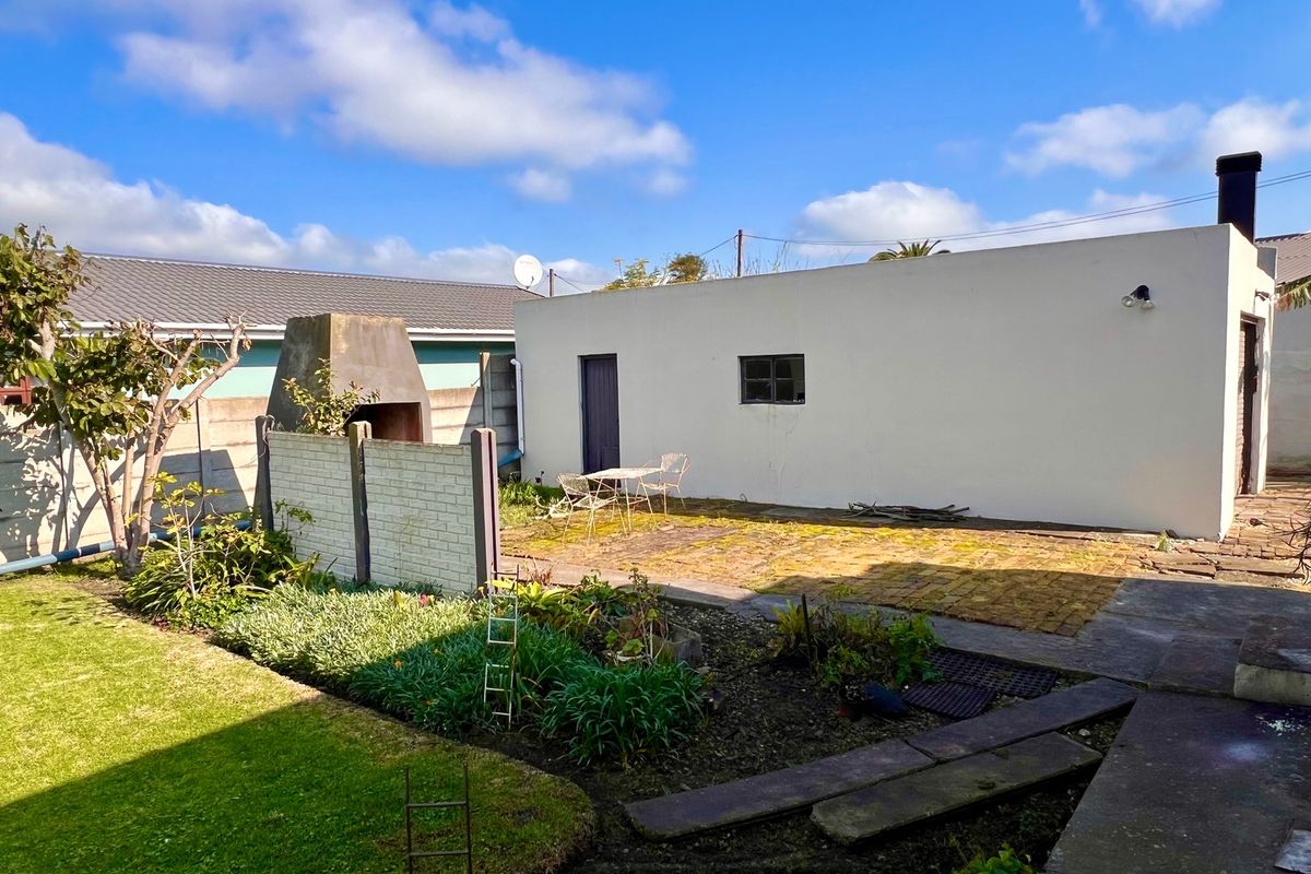 Rear garden area featuring a paved patio, built-in braai, and established garden beds, offering potential for outdoor entertainment space.