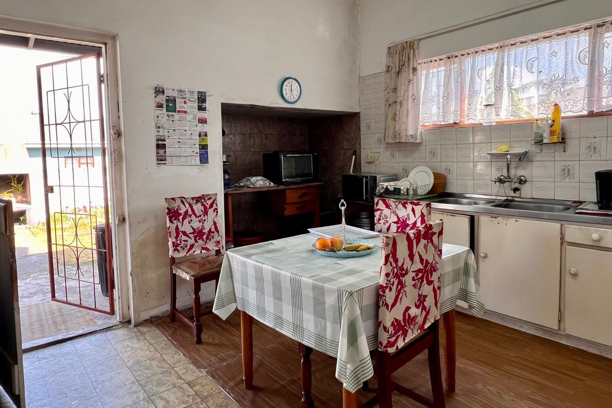 A dated kitchen featuring tiled splashbacks, built-in cabinetry, and a stainless steel sink, with direct access to the exterior via a security gate.