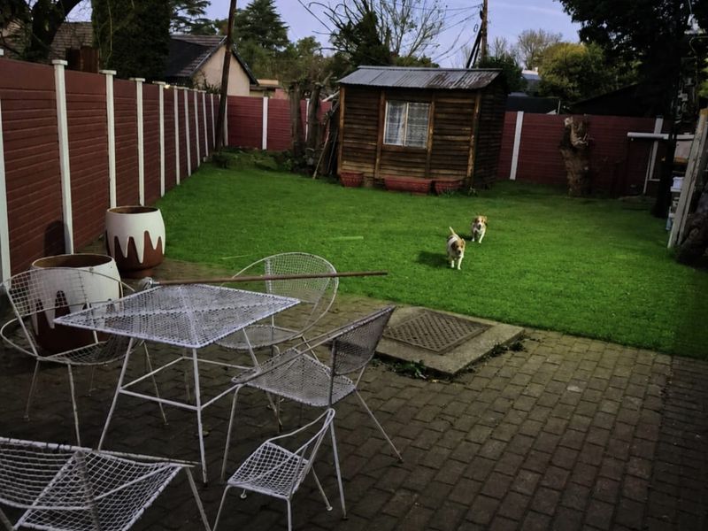 A private rear garden featuring a paved patio area, a lawn, and a timber storage shed enclosed by perimeter fencing.