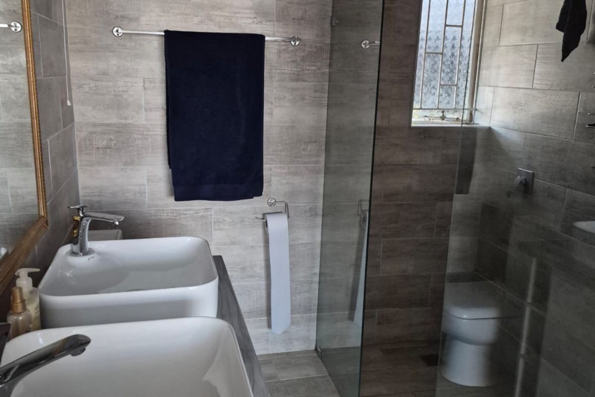 Modern bathroom featuring a double vanity with vessel sinks, a spacious glass-enclosed shower with a rain shower head, and contemporary tiled finishes.