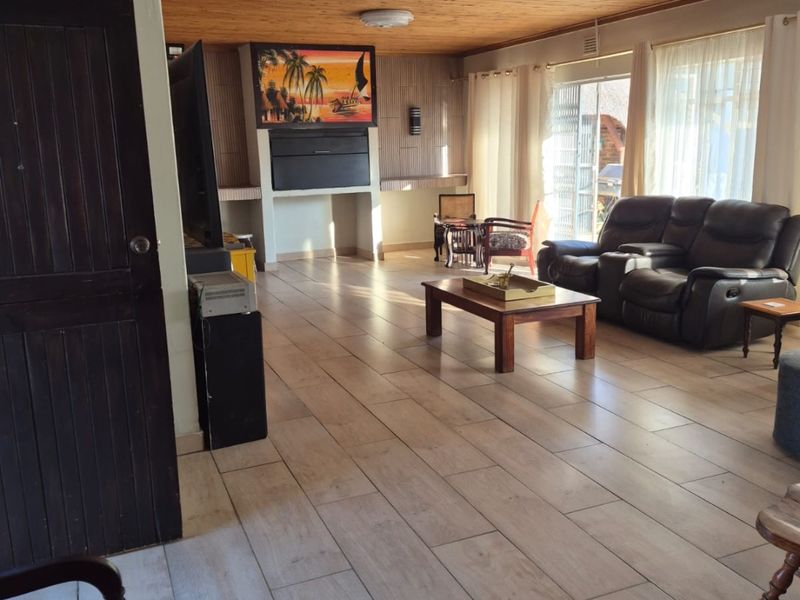 Spacious living room featuring wood-paneled ceilings, tiled flooring, and a built-in fireplace, with direct access to the outdoor area through sliding glass doors.
