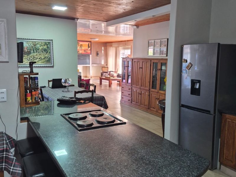 Open-plan living and kitchen area featuring a granite island with integrated hob, timber ceiling finishes, and tiled flooring throughout.