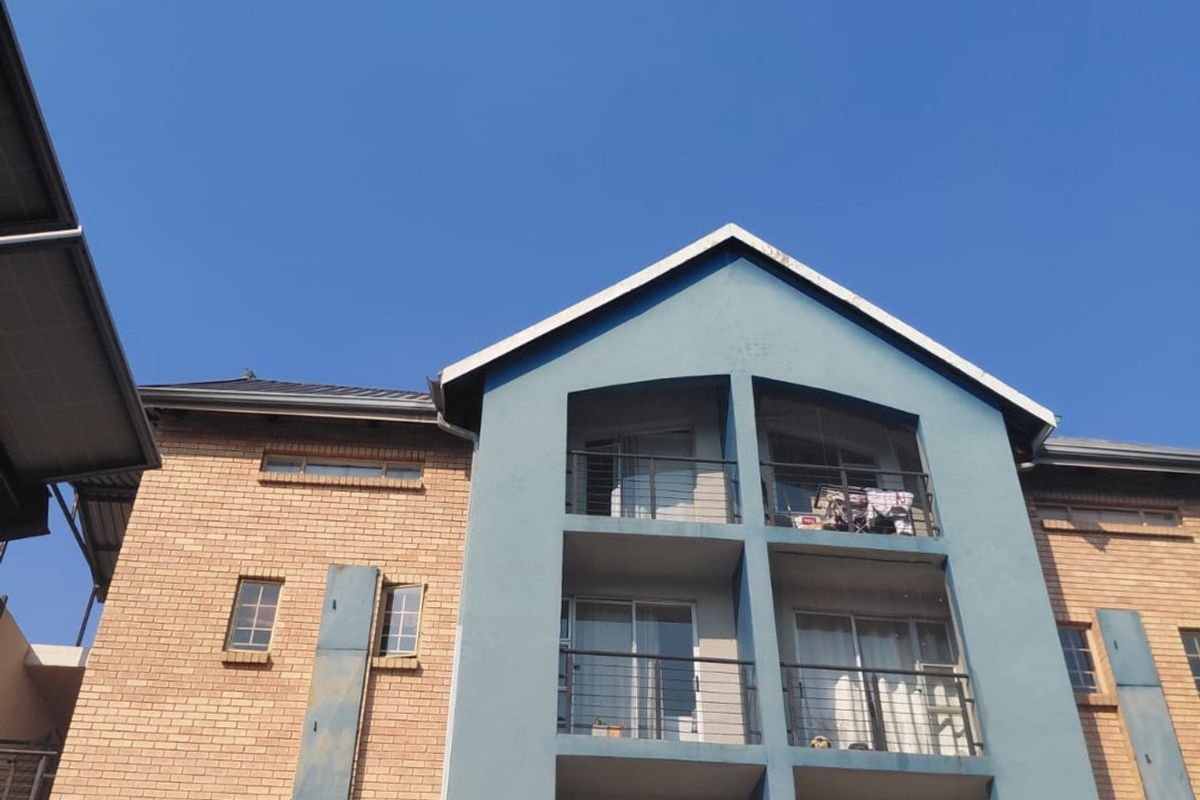 Exterior view of a multi-story apartment building featuring brick cladding, blue painted accents, and private balconies with sliding glass doors.