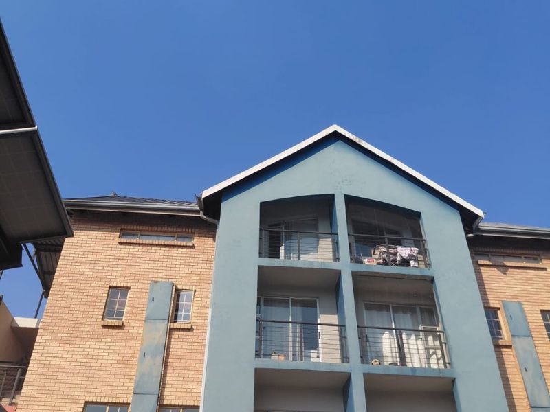 Exterior view of a multi-story apartment building featuring brick cladding, blue painted accents, and private balconies with sliding glass doors.