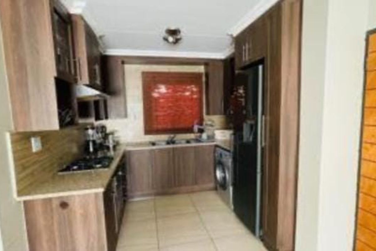 A compact galley-style kitchen featuring wood-finish cabinetry, granite countertops, a gas hob, and integrated laundry plumbing.