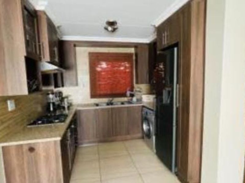 A compact galley-style kitchen featuring wood-finish cabinetry, granite countertops, a gas hob, and integrated laundry plumbing.