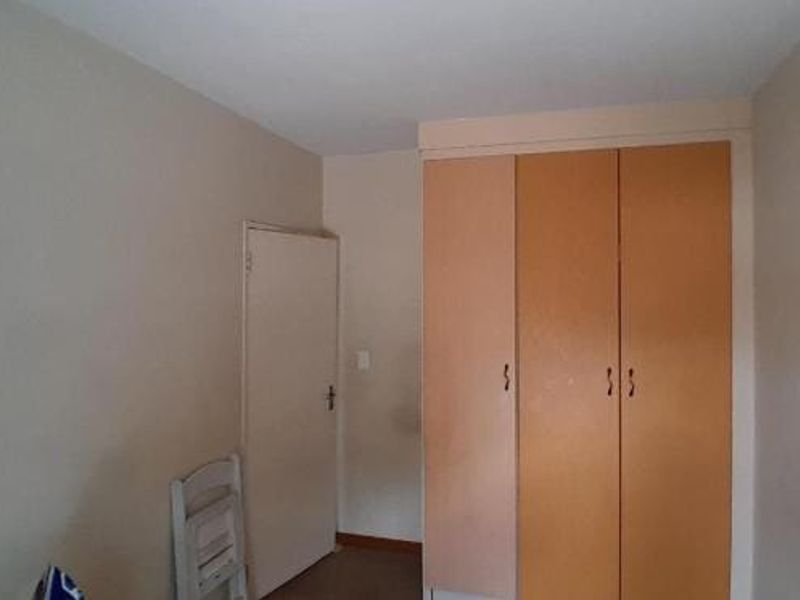 A simple bedroom featuring neutral walls and functional built-in wooden cupboards, offering a clean and versatile space.