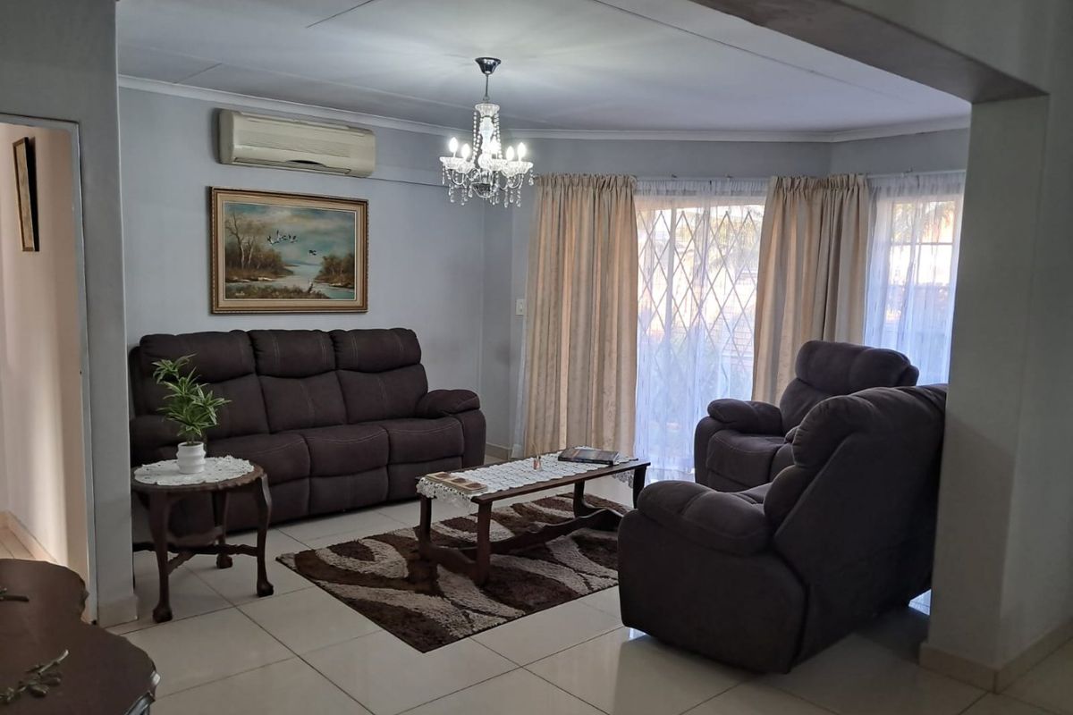 A comfortable living room featuring tiled flooring, a split-system air conditioner, and large sliding glass doors with security gates providing natural light.