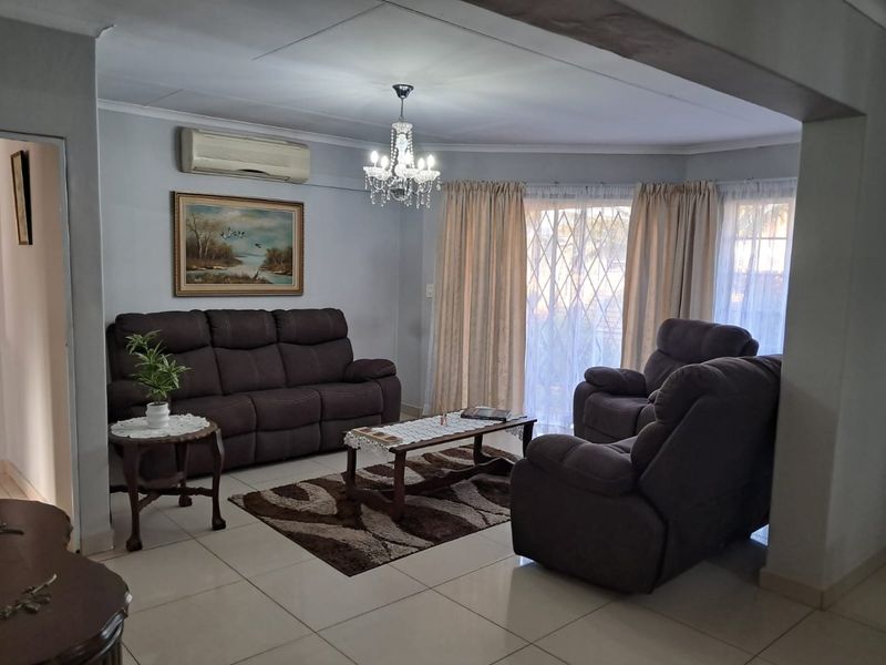 A comfortable living room featuring tiled flooring, a split-system air conditioner, and large sliding glass doors with security gates providing natural light.
