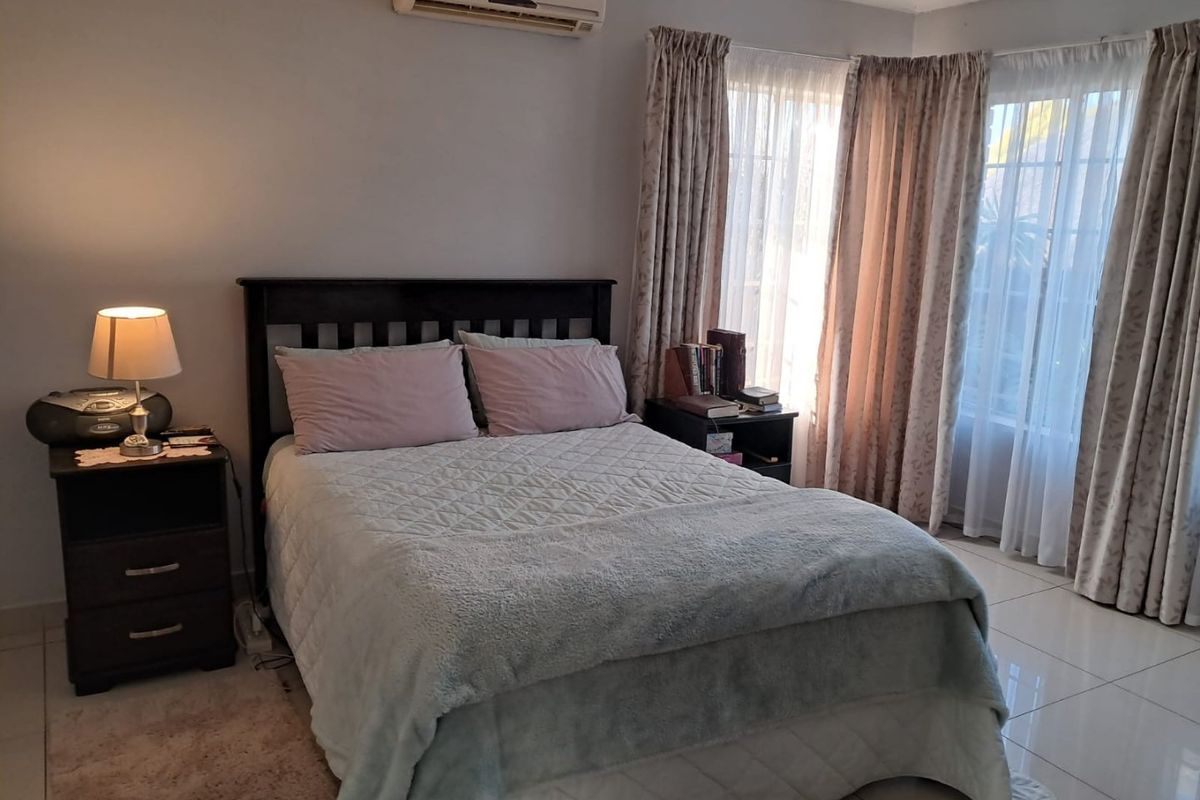 A functional bedroom featuring tiled flooring and a wall-mounted air conditioning unit, offering a comfortable and well-lit space.