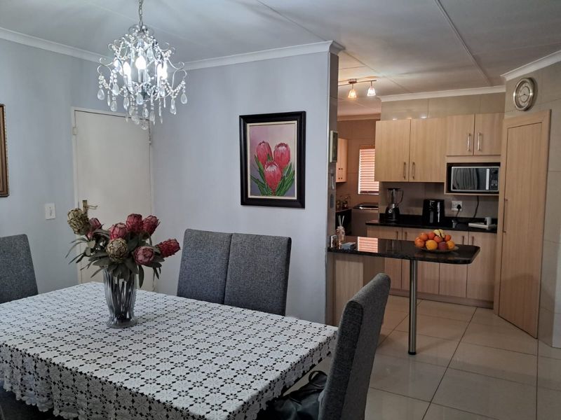 Open-plan dining area featuring a crystal chandelier, seamlessly connected to a functional kitchen with built-in cabinetry, granite countertops, and tiled flooring throughout.