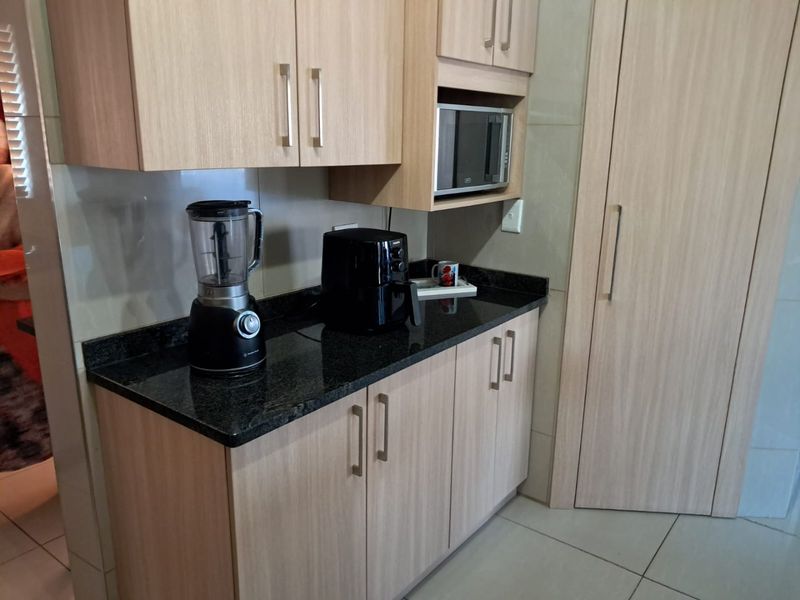 A compact kitchen area featuring light wood-finish cabinetry, dark granite countertops, and a built-in microwave, complemented by neutral tiled flooring.