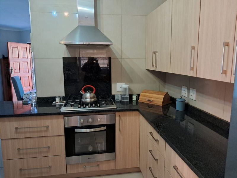 A well-maintained kitchen featuring light wood cabinetry, black granite countertops, and integrated stainless steel appliances including a gas hob and extractor fan.