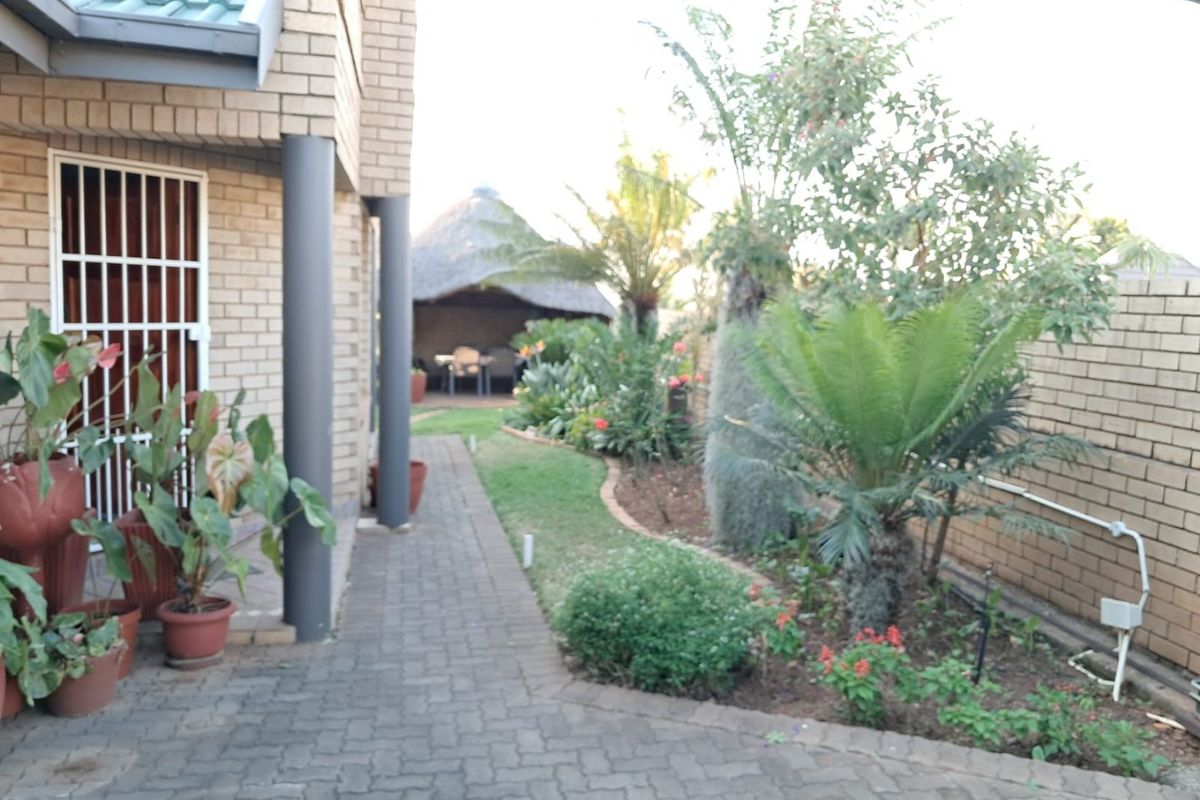 A well-maintained rear garden area featuring brick paving, established landscaping, and a thatched lapa structure for outdoor entertainment.