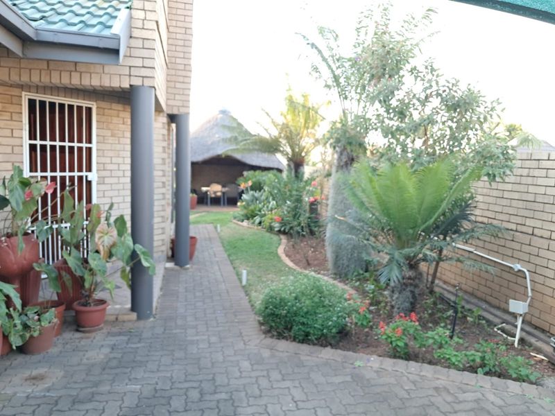 A well-maintained rear garden area featuring brick paving, established landscaping, and a thatched lapa structure for outdoor entertainment.