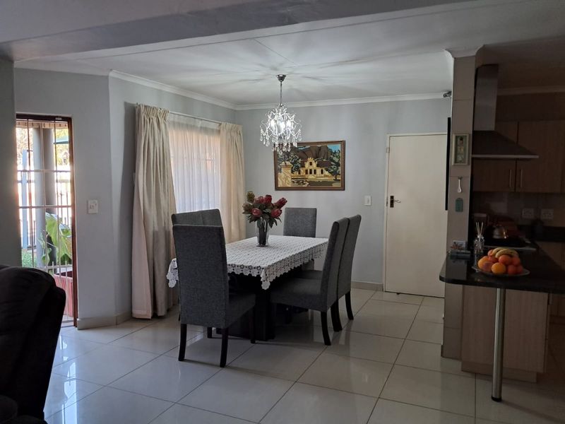 Open plan dining area featuring tiled floors, a crystal chandelier, and direct access to an outdoor patio, adjacent to a modern kitchen.